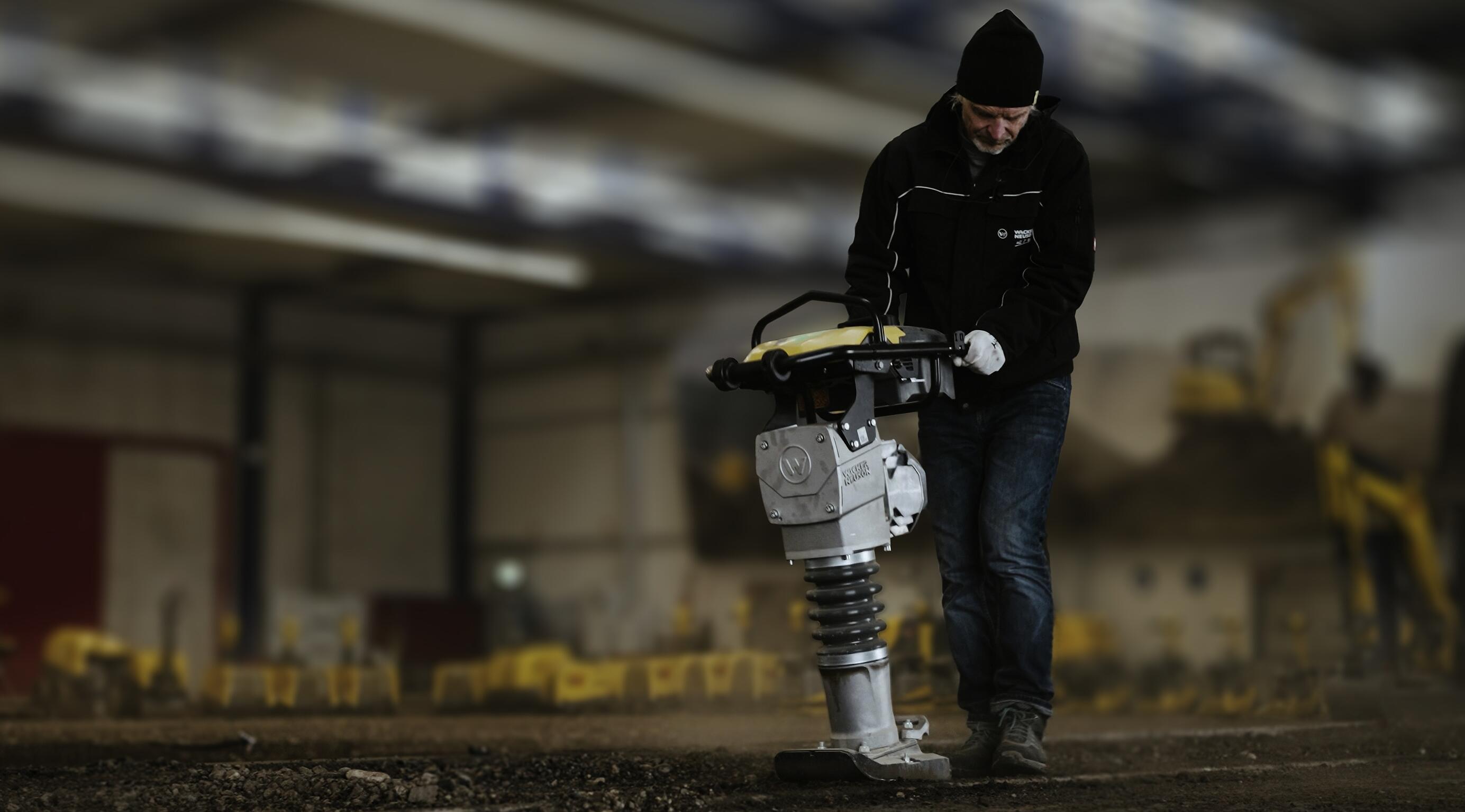 Munkás, aki talajtömörítő döngölőt kezel egy beltéri építőipari gyakorlóteremben