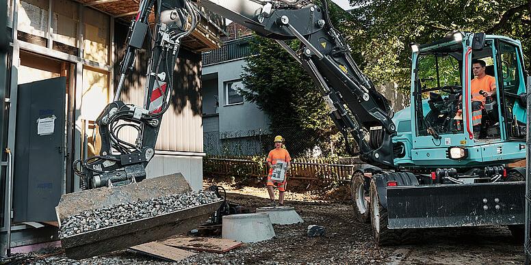 A Wacker Neuson EW100 kerekes kotrógép billenőkanállal ömlesztett anyagot mozgat egy építkezésen.