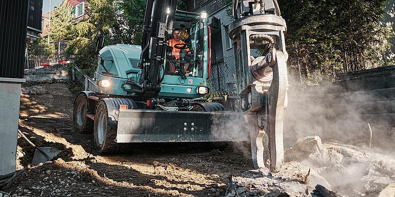 A Wacker Neuson EW100 kerekes kotrógép hidraulikus kalapáccsal végzi a bontási munkálatokat egy szűk lakóövezetben.