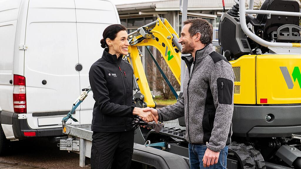 Wacker Neuson employee shaking a customer’s hand in front of a Wacker Neuson zero emission tracked excavator.