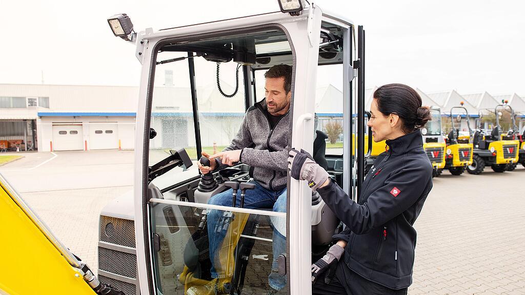 Wacker Neuson employee advising customer sitting in a Wacker Neuson tracked excavator on the classic range of rentals at Wacker Neuson.