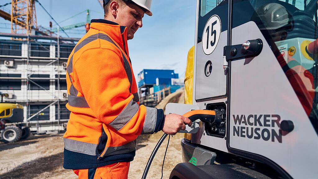 A man connects a charging cable to an electric wheel loader to charge it